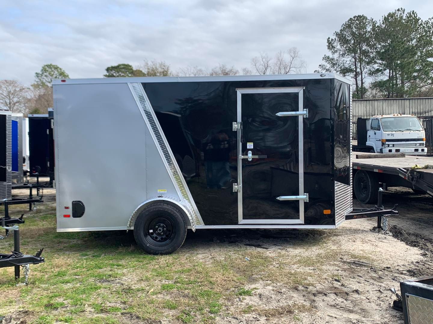 A black and silver enclosed cargo trailer with a side door, parked outside on grass.