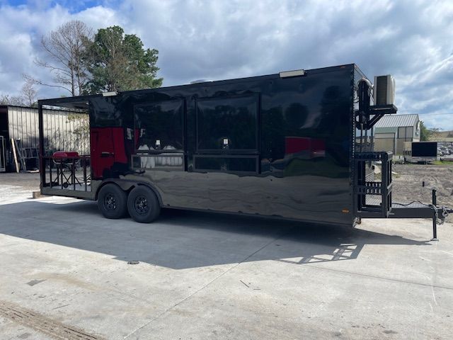 Black food trailer on a paved surface. It has a serving window with a grill.