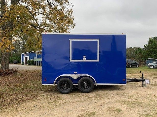 Blue food trailer with a serving window, parked on grass.