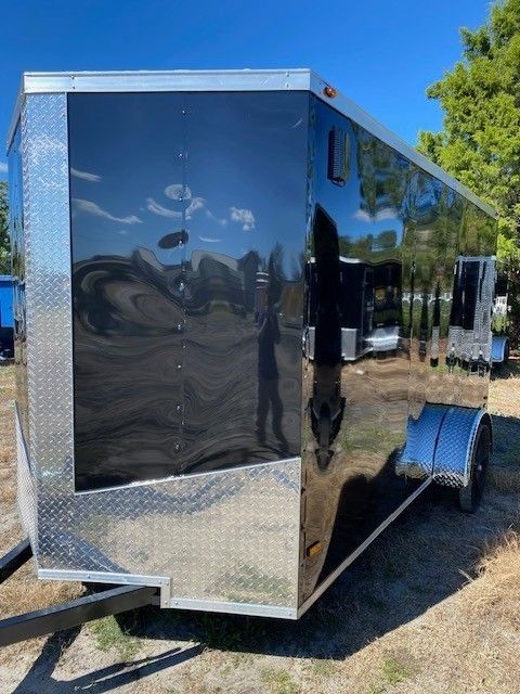 Black enclosed trailer with diamond plate accents, parked outdoors on grass.