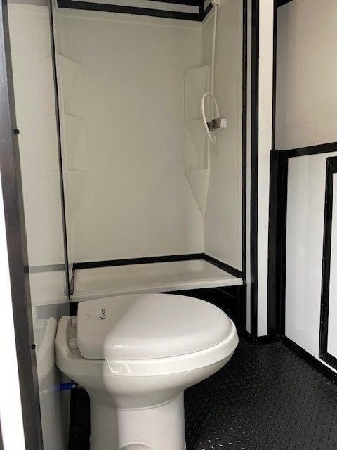 Interior of a mobile restroom, white toilet below a shower stall. Black and white color scheme.