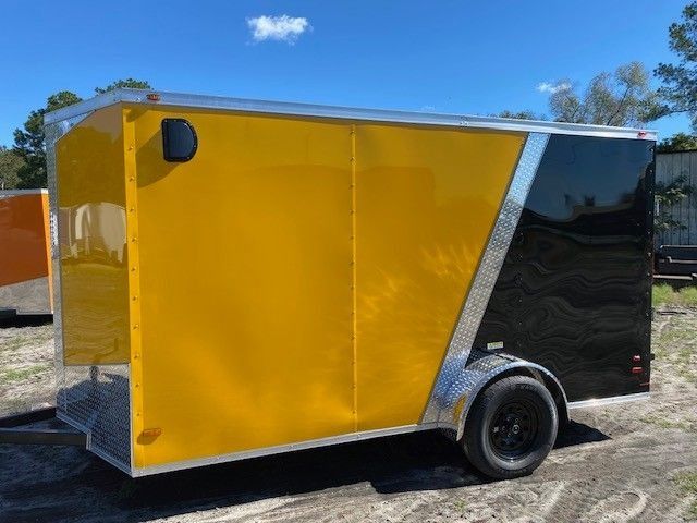 Yellow and black enclosed trailer with a black wheel against a blue sky.