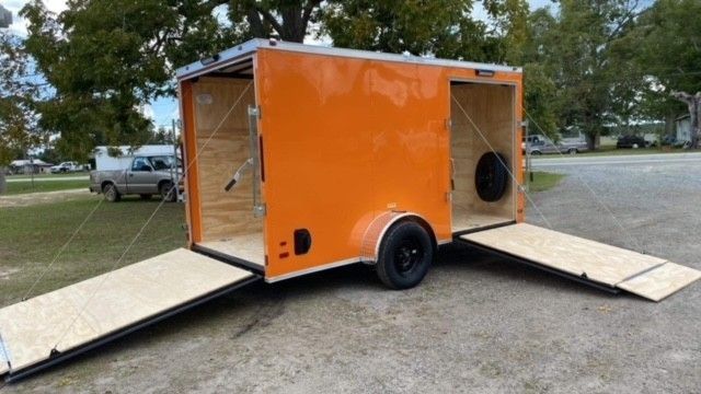 Orange cargo trailer with open doors and ramps, parked outdoors.