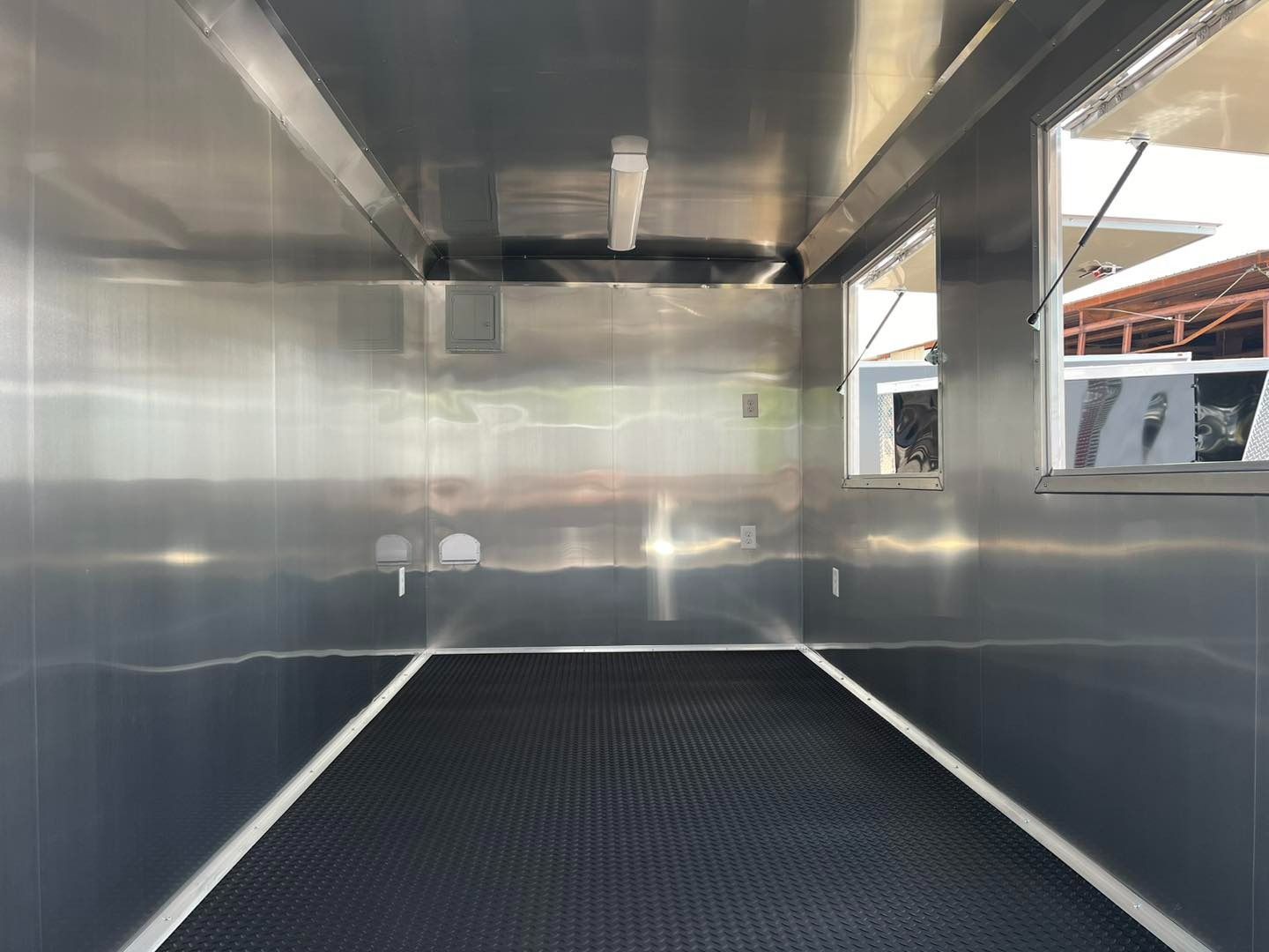 Empty stainless steel food truck interior with black flooring and windows.