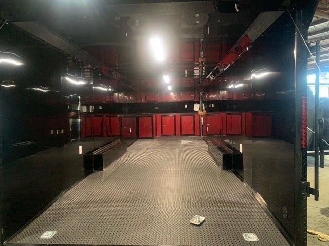 Interior view of an empty black race car trailer with red storage cabinets and metal flooring.