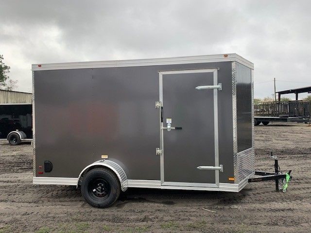 Dark gray enclosed cargo trailer, side view, door open, wheels on dirt.