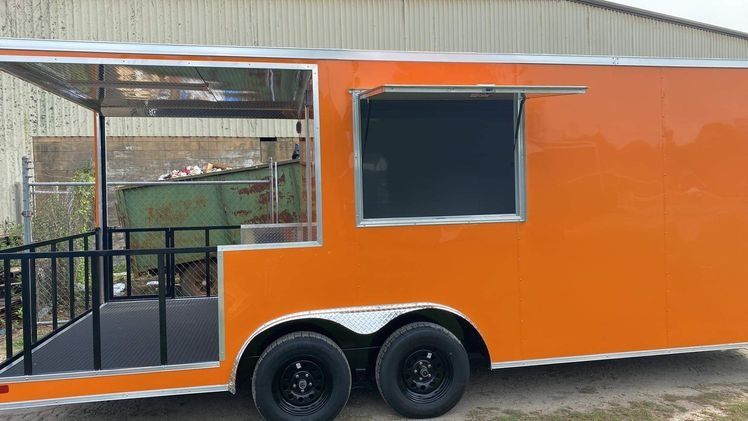 Orange food trailer with black tires, ramp, and serving window.