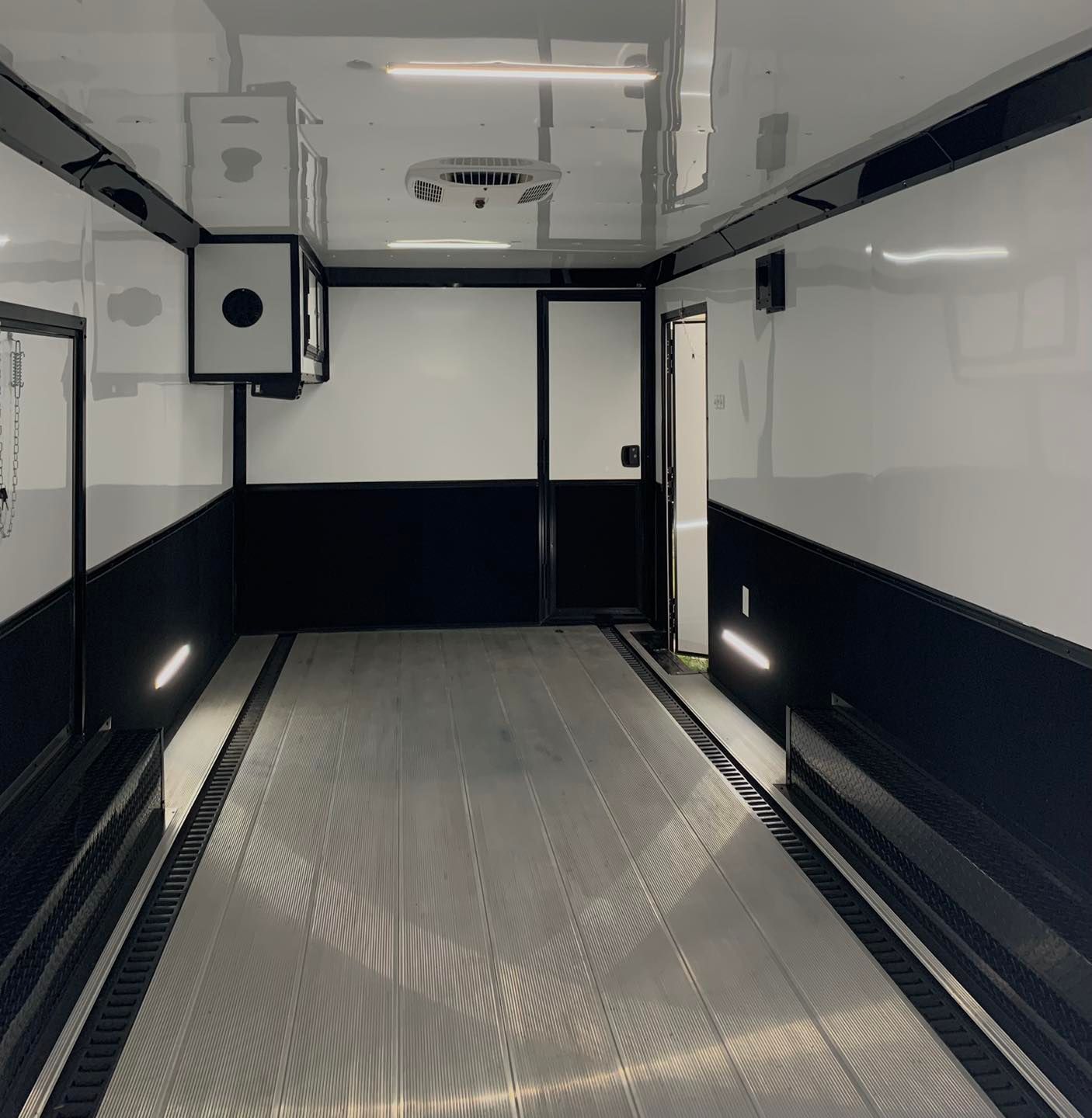 Interior of a black and white trailer with a shiny floor, air conditioning, and a door.