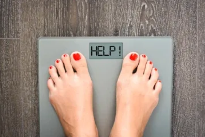 Feet with red toenails stand on a scale displaying