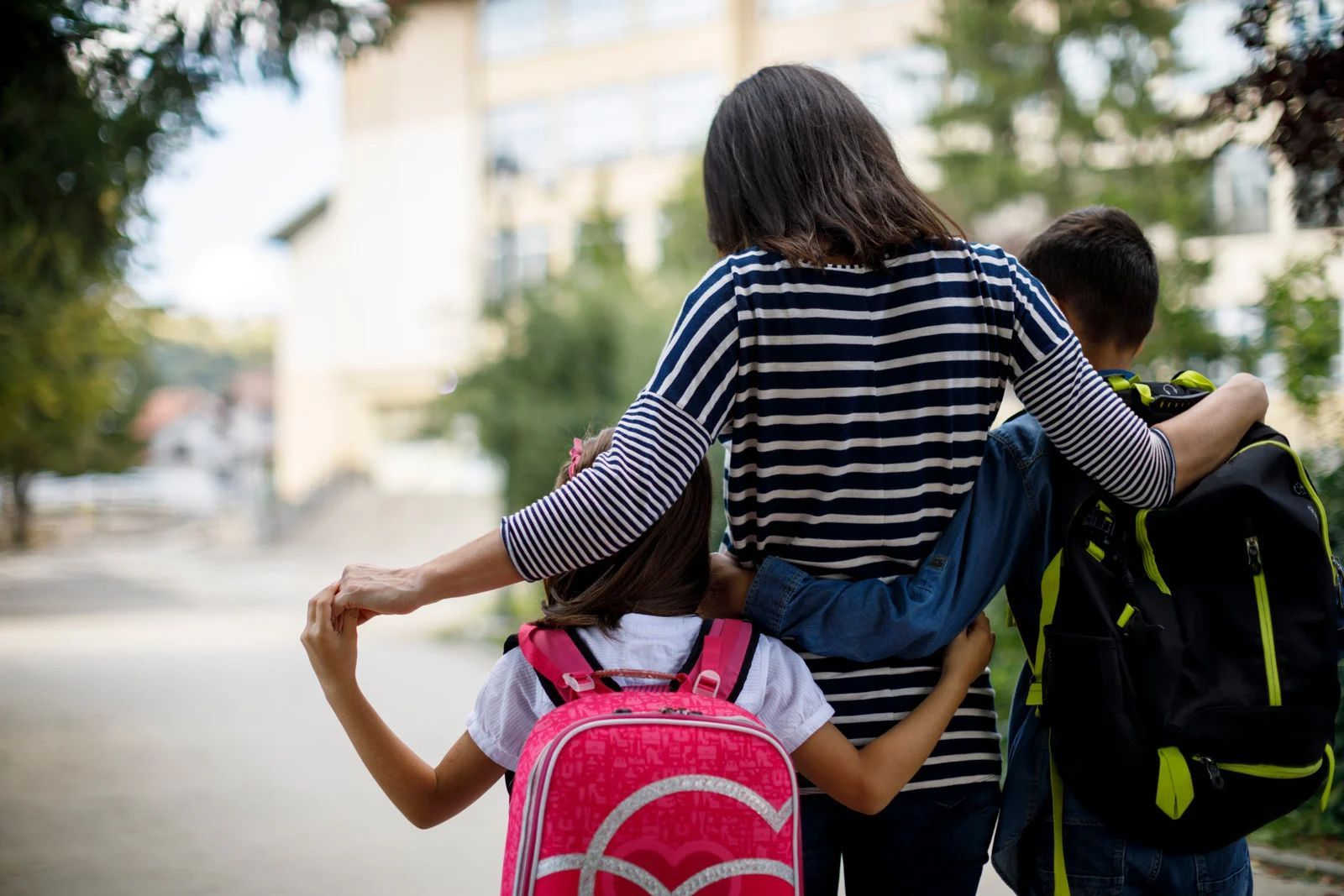 Three children with backpacks walking together outdoors on a path