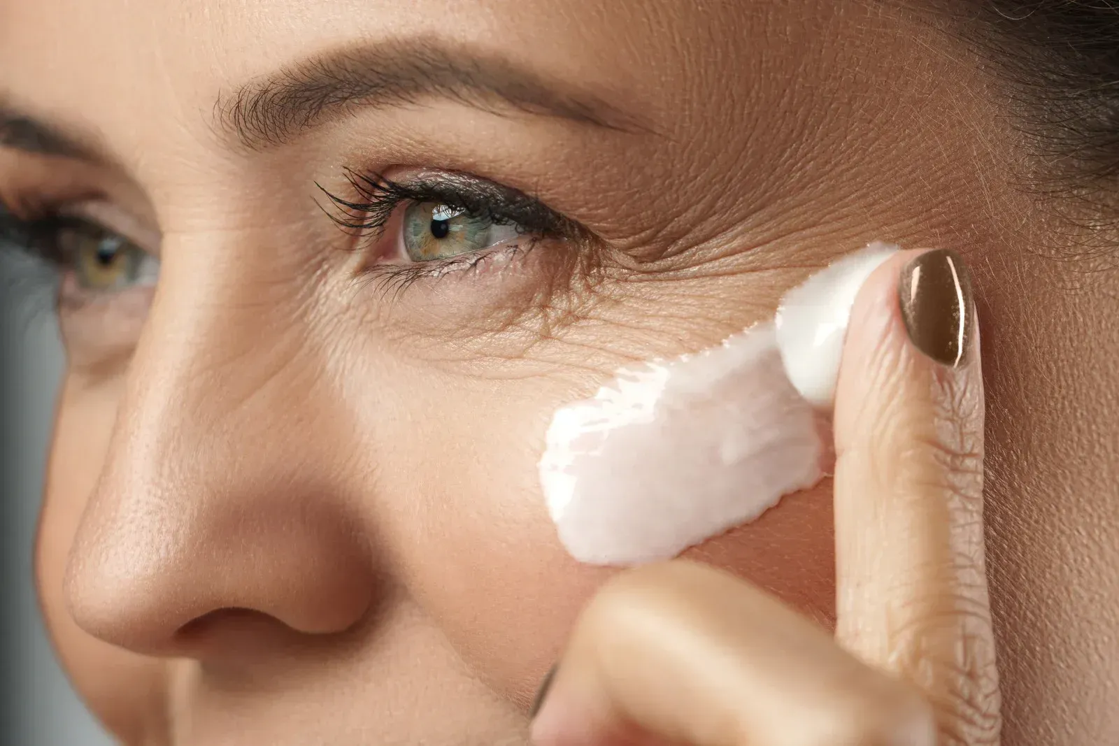 Woman applying cream to her face, focusing on wrinkles around her eye.