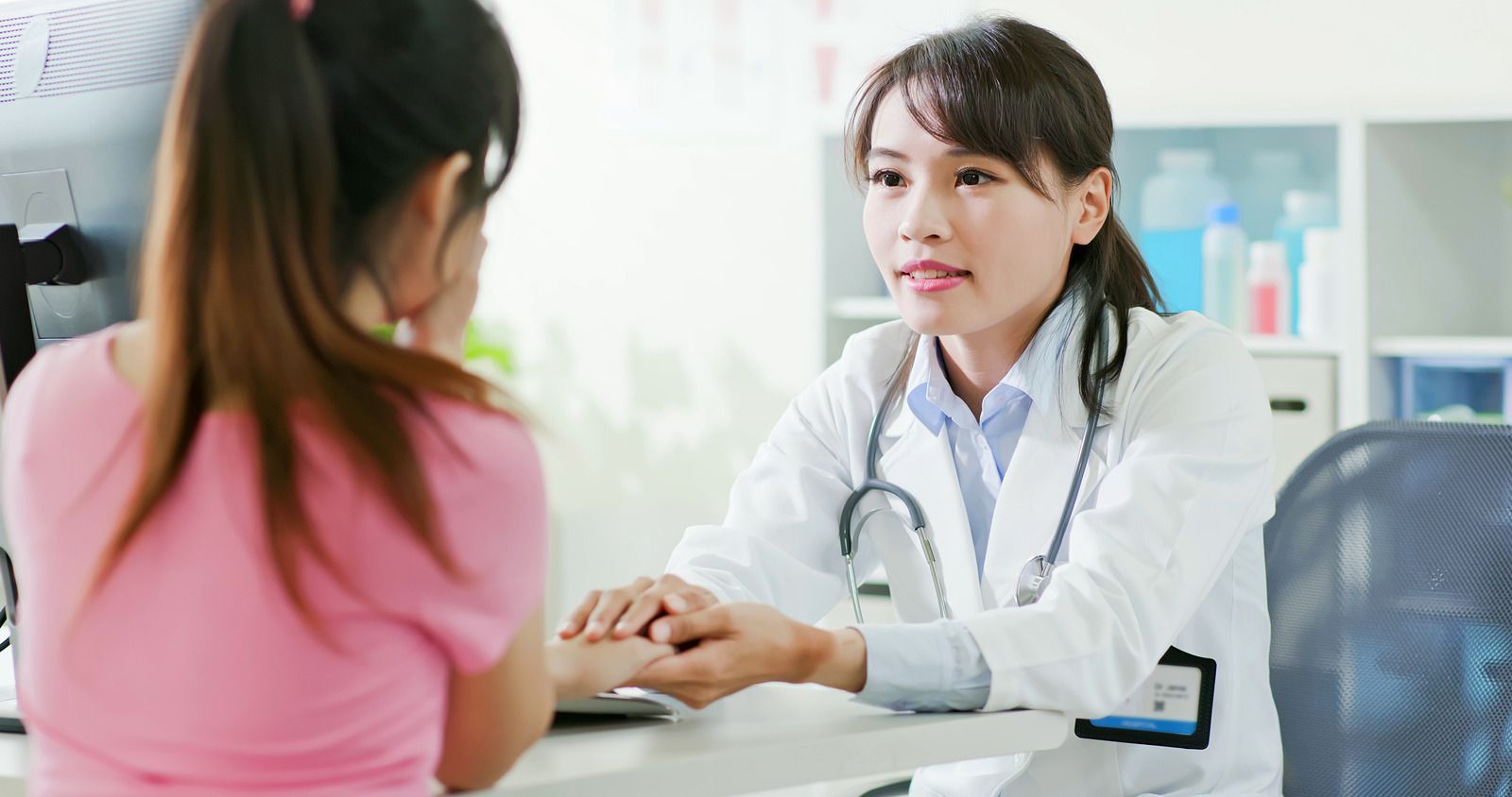 Doctor speaking with a patient across a desk in a bright clinic office