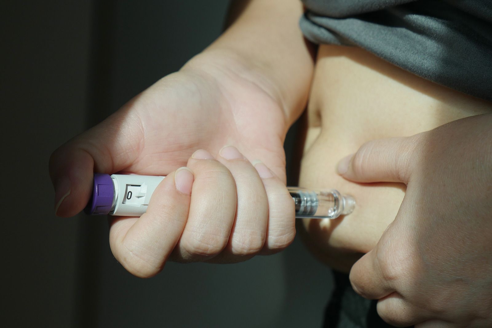 Hands holding a syringe near an abdomen, preparing an injection