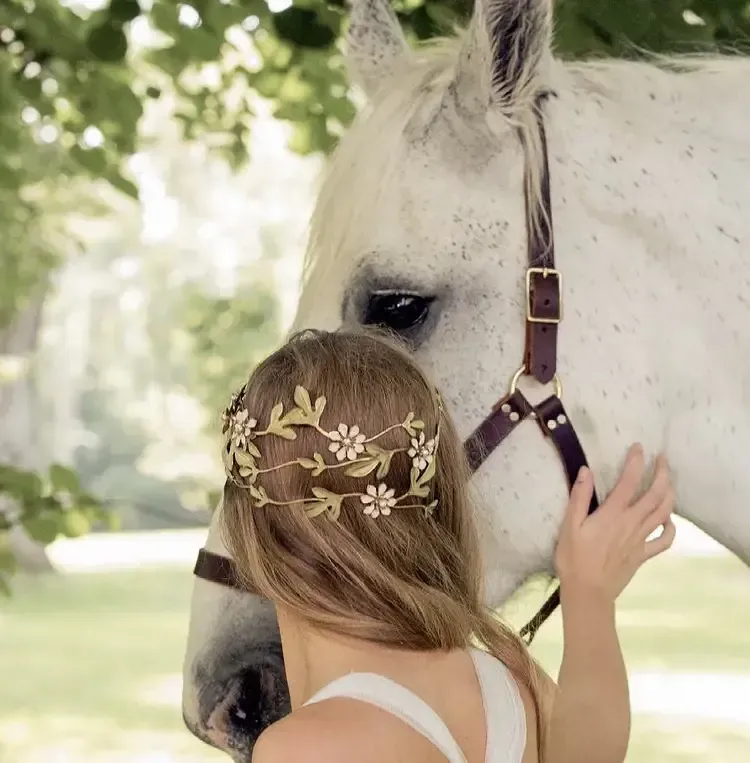 A woman wearing a flower crown is petting a white horse.