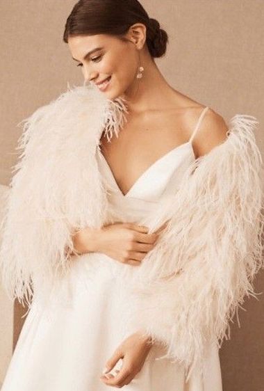 A woman in a white dress is wearing a white feathered jacket.