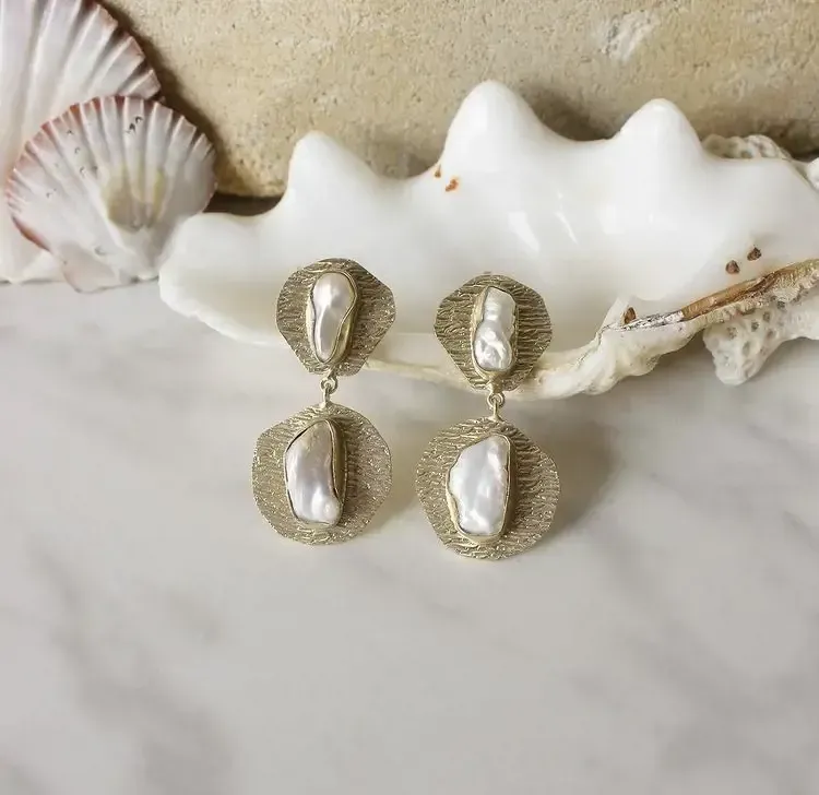 A pair of earrings are sitting on top of a sea shell.