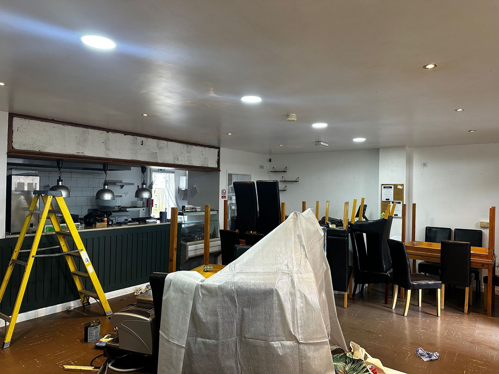 A large room with tables and chairs and a ladder.