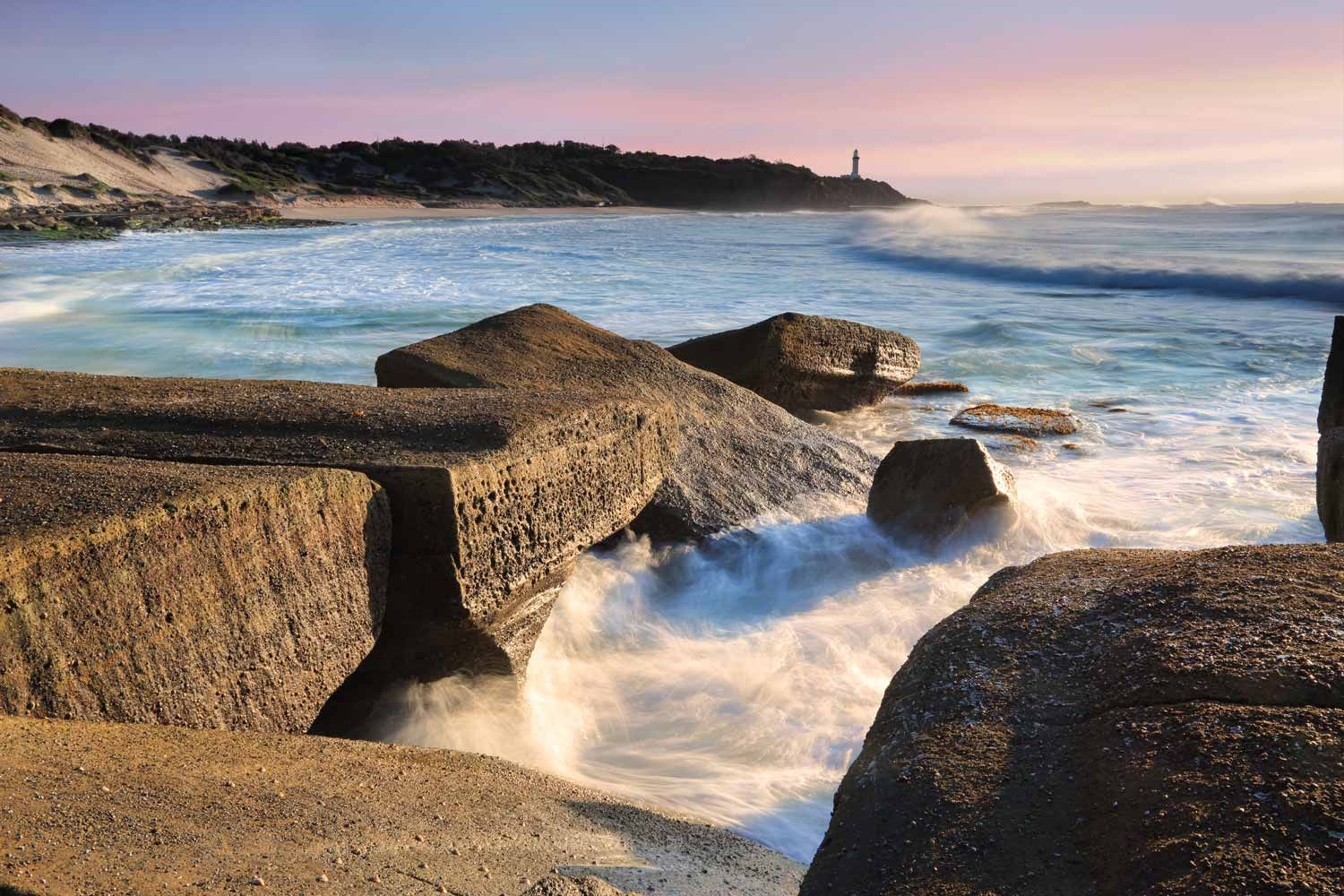 Ocean waves crash against large, angular rocks at sunset — Easy Mix Concrete In Central Coast, NSW