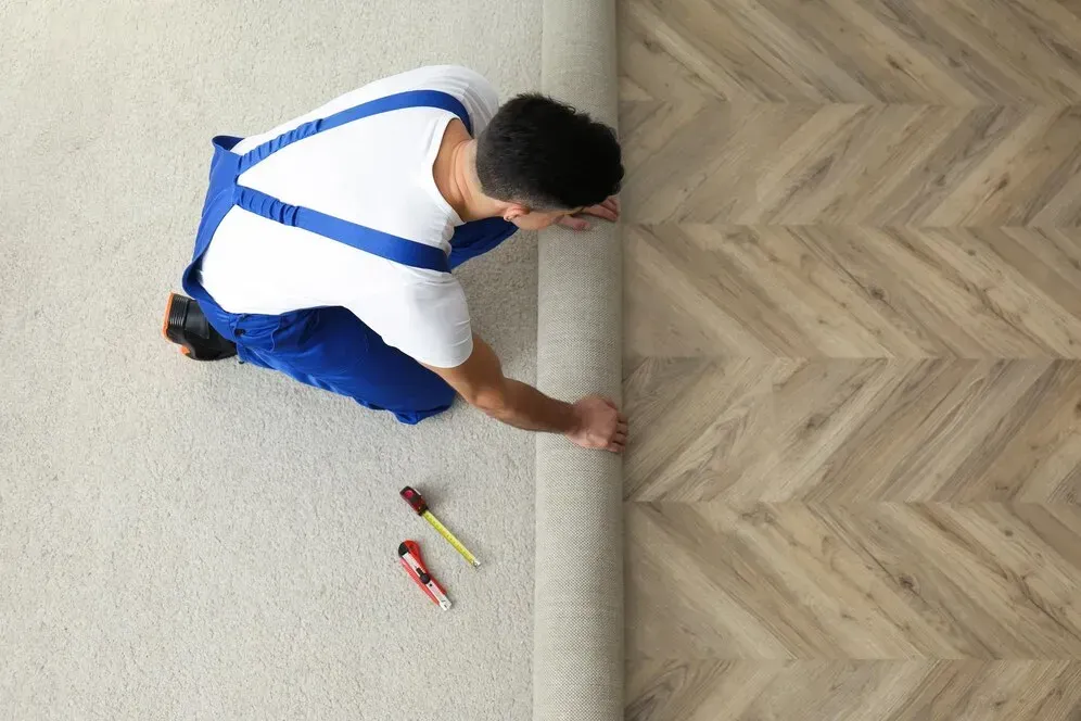 A man is installing a carpet on a wooden floor.
