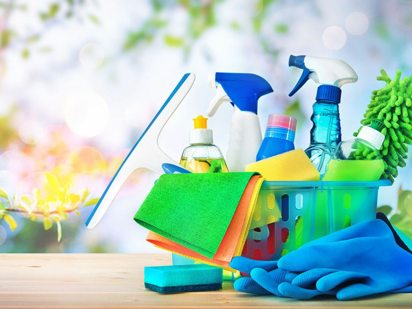 Cleaning supplies in a caddy with spray bottles, cloths, gloves, and a squeegee on a table