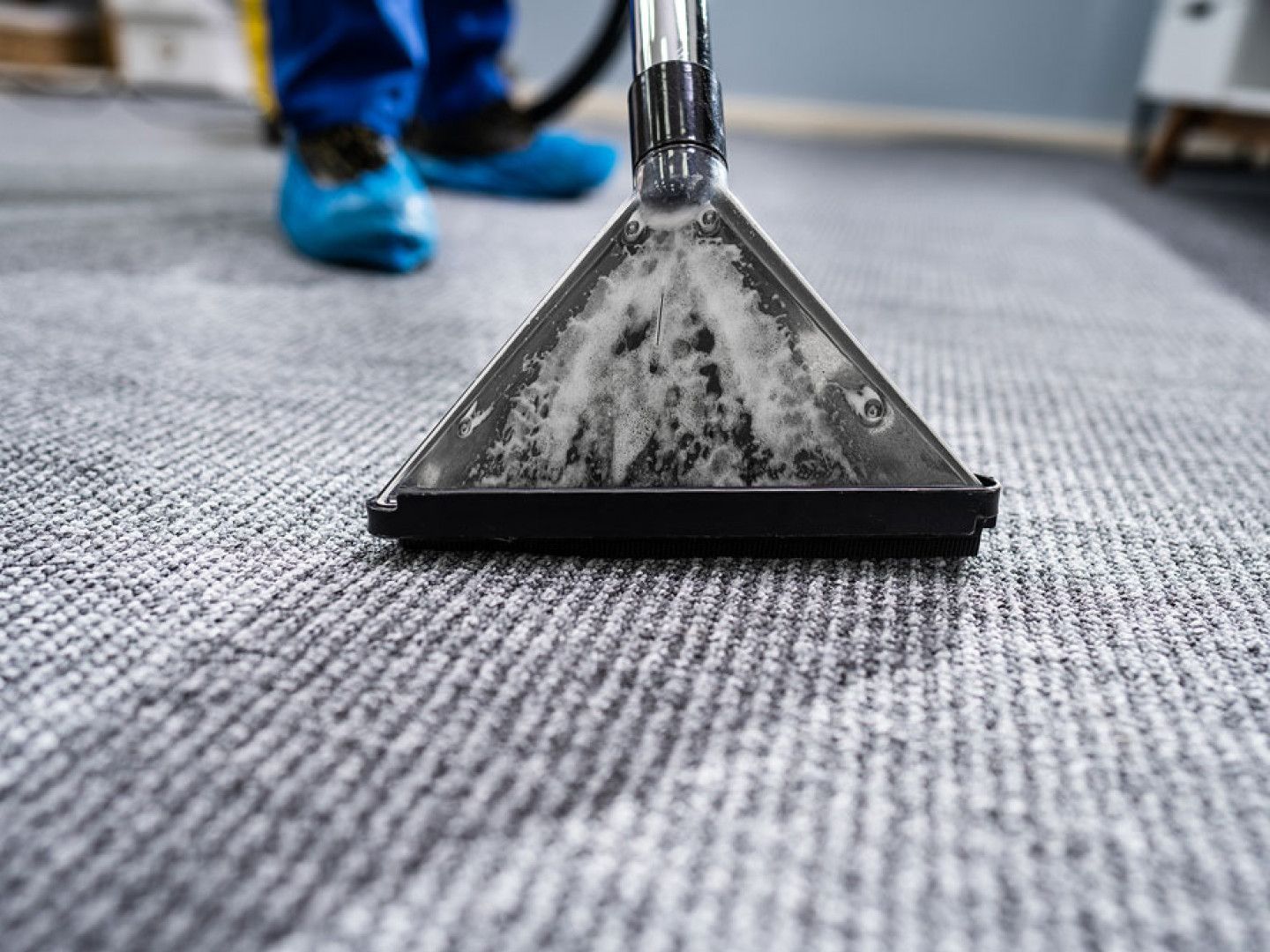Carpet cleaning nozzle on gray rug, with a person in blue shoes behind it