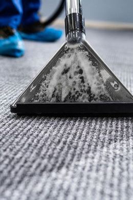 Carpet cleaner head scrubbing a gray carpet, with a blue shoe blurred in the background