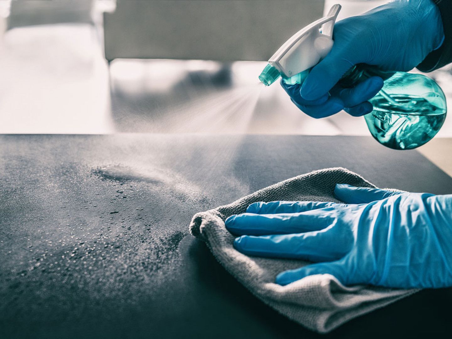 Gloved hand spraying disinfectant and wiping a surface with a cloth