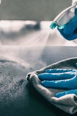 Blue-gloved hands spray disinfectant onto a cloth during surface cleaning.