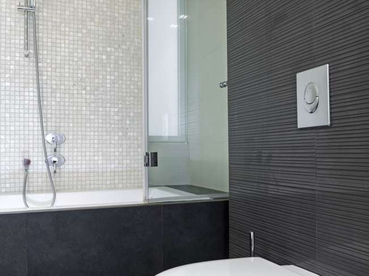 Modern bathroom with a bathtub, glass shower partition, mosaic tile wall, and dark textured accent wall.