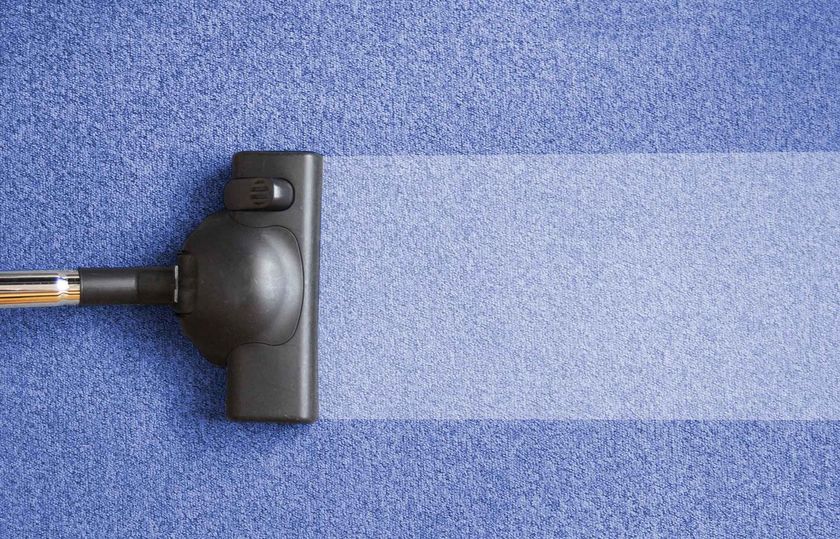 Vacuum cleaner head on a patterned carpet with a person’s shoes in the background