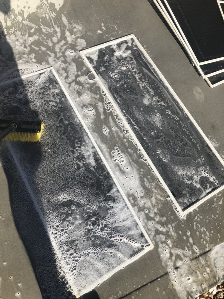 Gloved hand cleaning a dark floor with white soap suds around rectangular panels