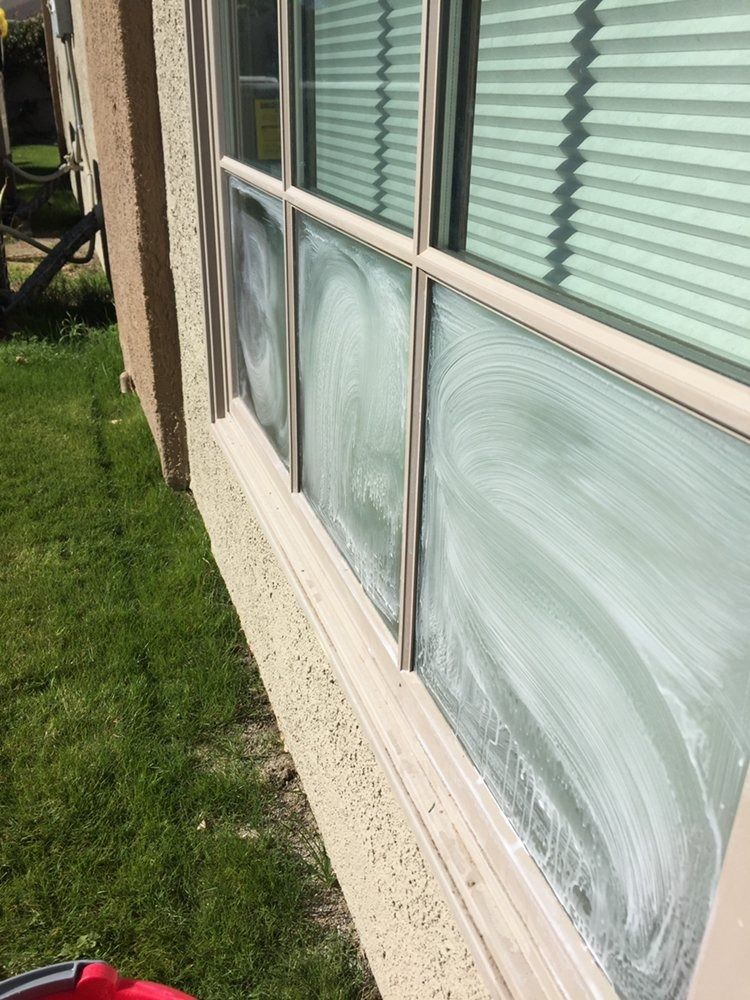 Exterior house window with white blinds and frosted lower panes beside a green lawn