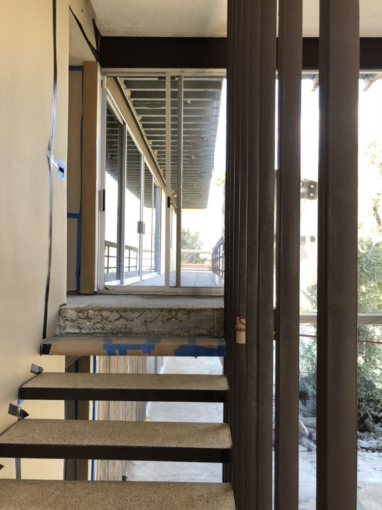 Stairway leading to a covered walkway beside a building, with glass doors and bright outdoor light.