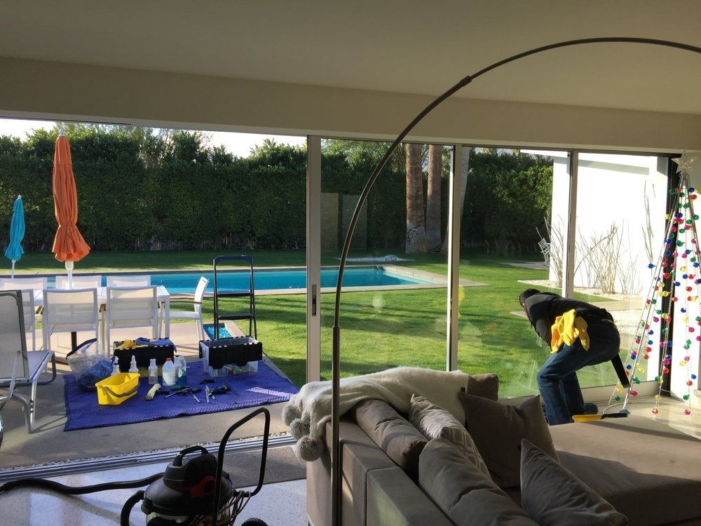 Person bending near a glass patio door by a pool, with outdoor furniture and patio umbrellas nearby.