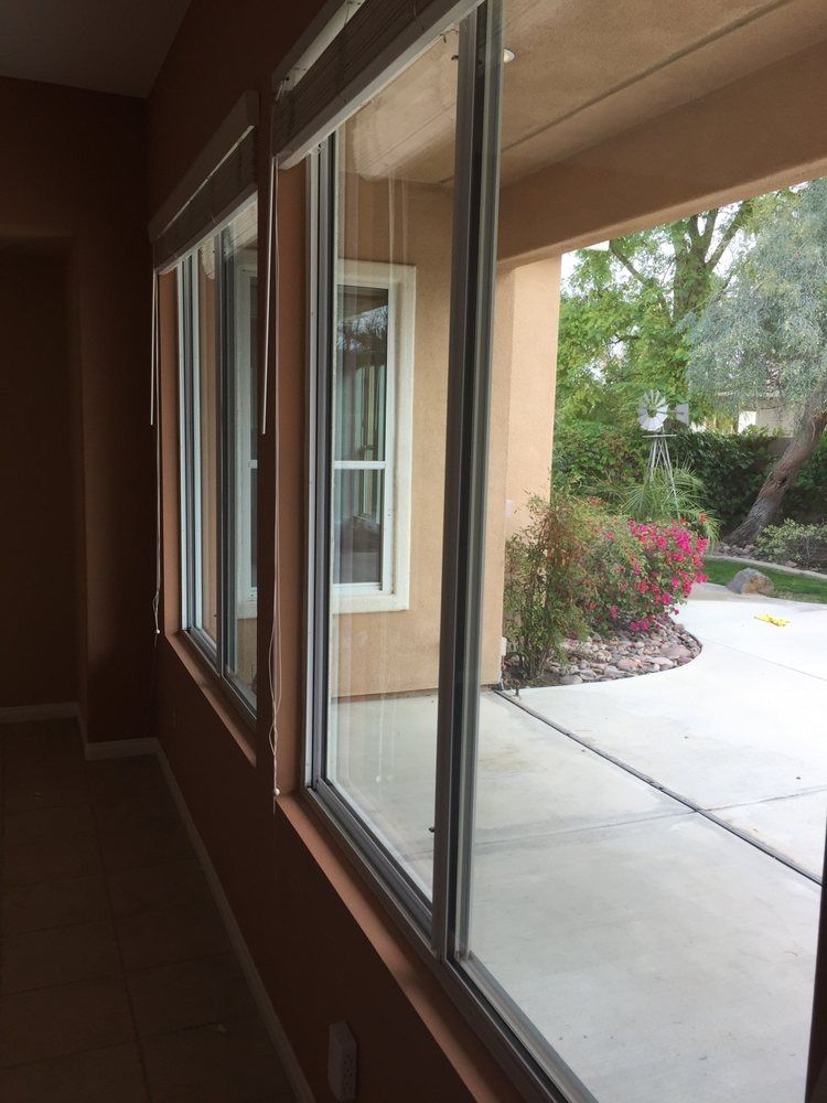View through a windowed porch to a concrete patio and shrubs outside.