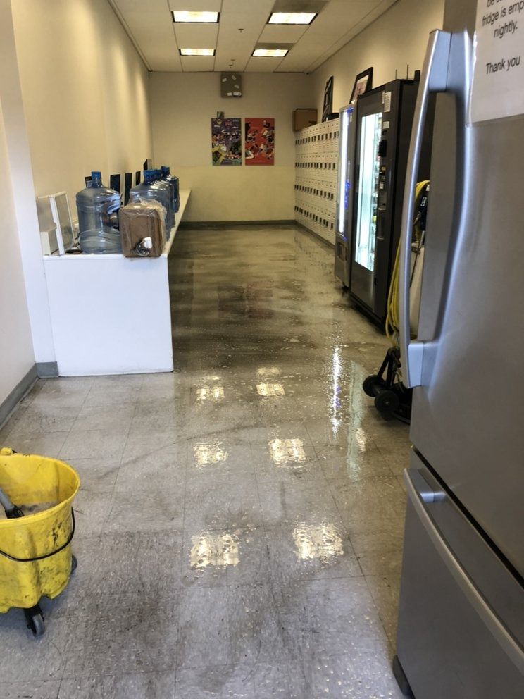 Hallway with vending machines, a stainless-steel fridge, and cleaning supplies on a wet, reflective floor.