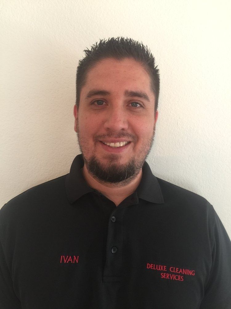 Smiling man in a black polo shirt standing against a plain wall
