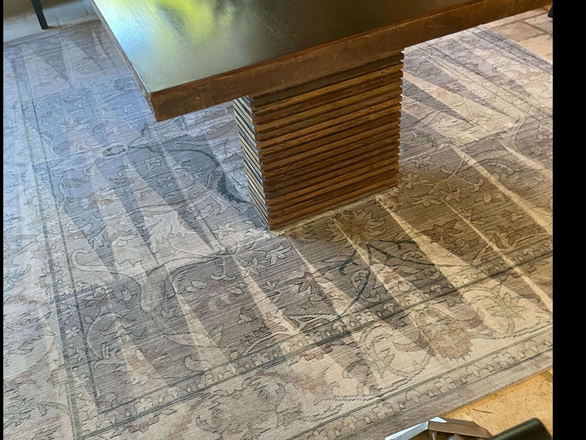 Patterned gray rug under a wood table with a glass top and wooden pedestal base.