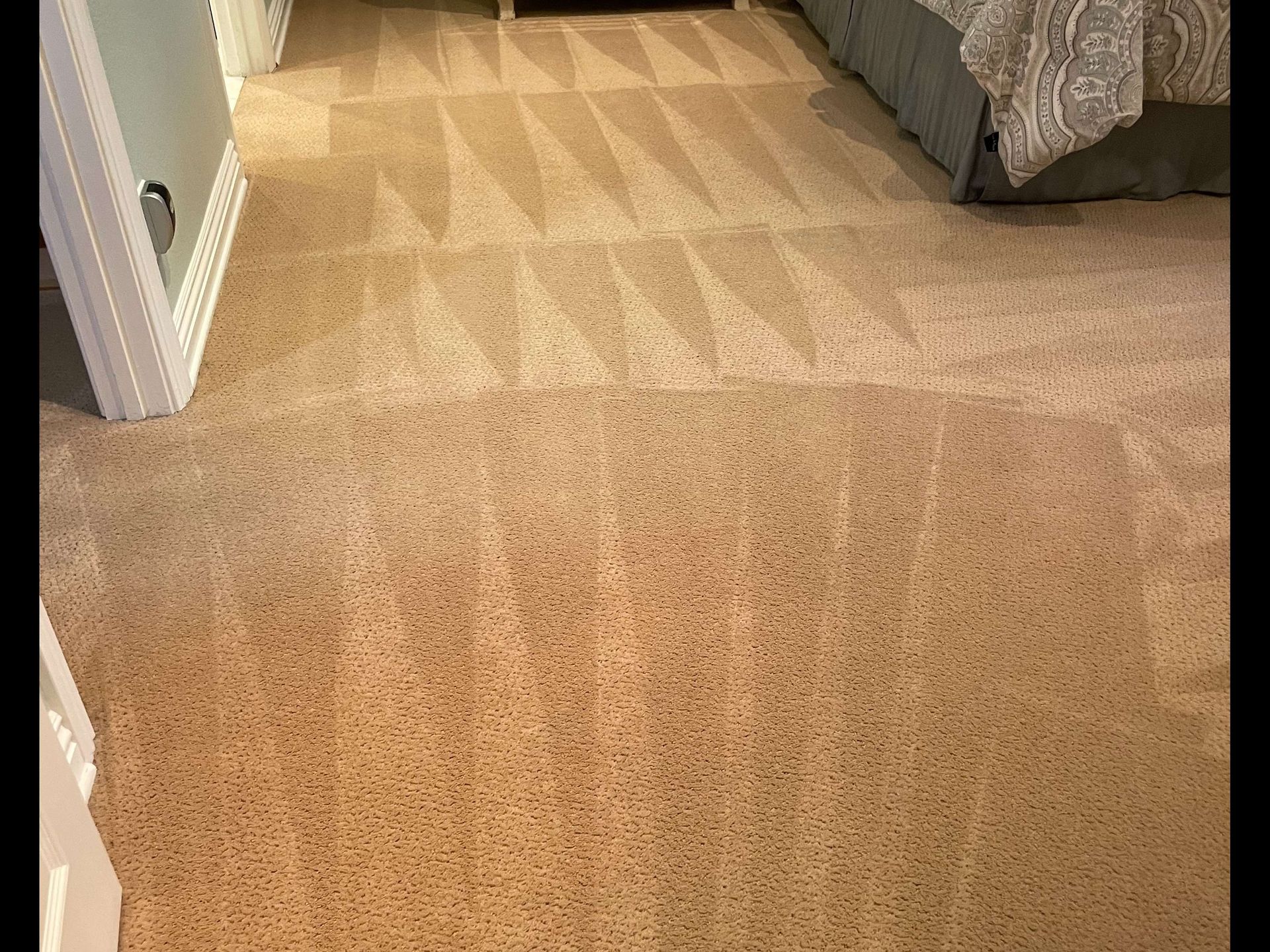 Carpeted hallway leading to a bedroom with a gray bed and patterned rug on the floor.