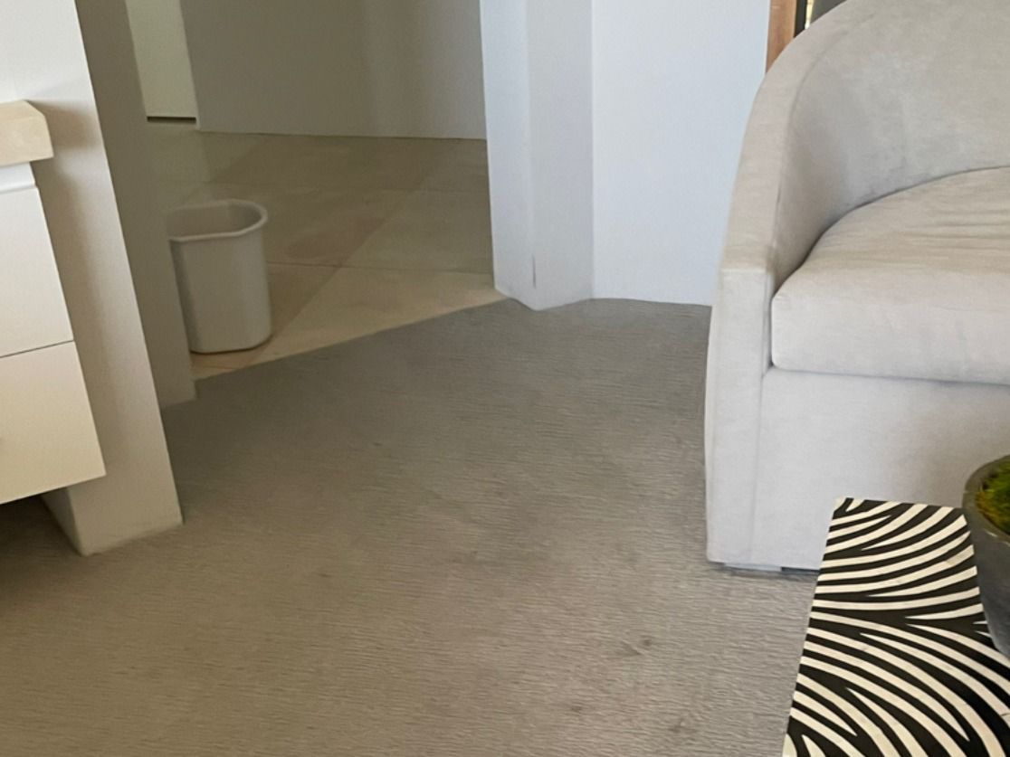 Carpeted living room corner with a beige sofa, white desk edge, and doorway to a hallway