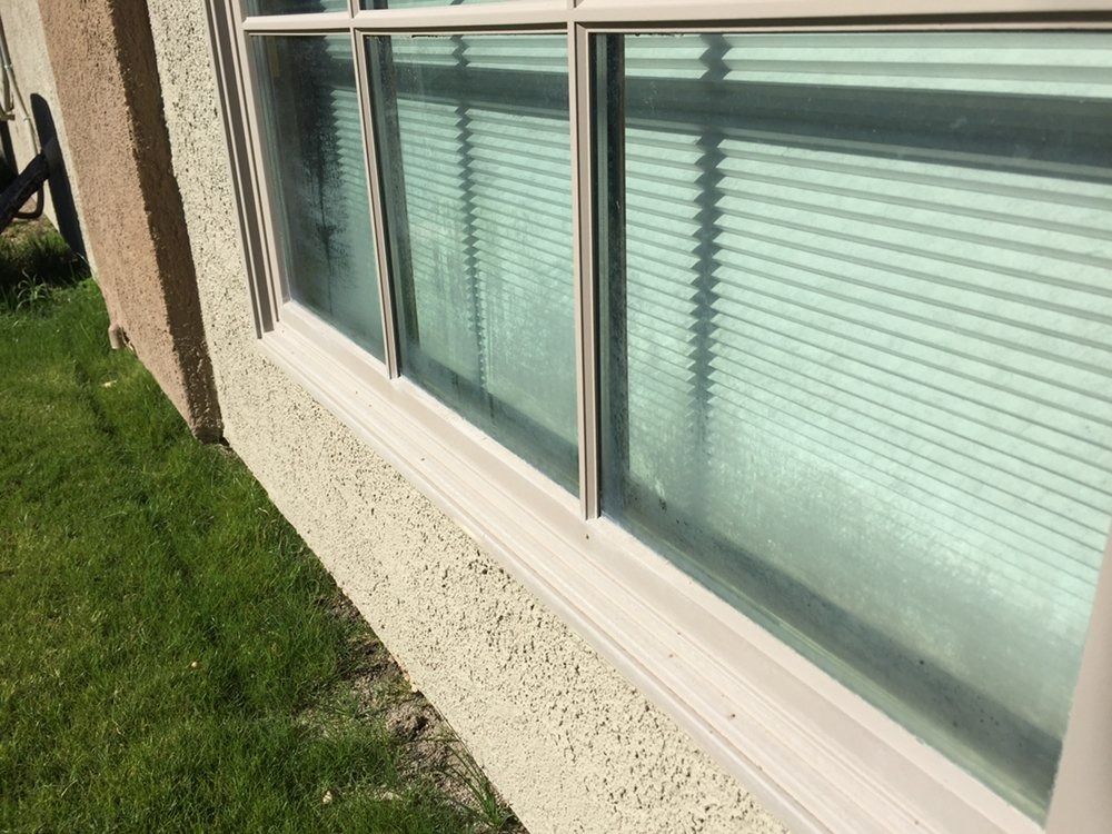 Side of a house with large windows and blinds beside a green lawn.