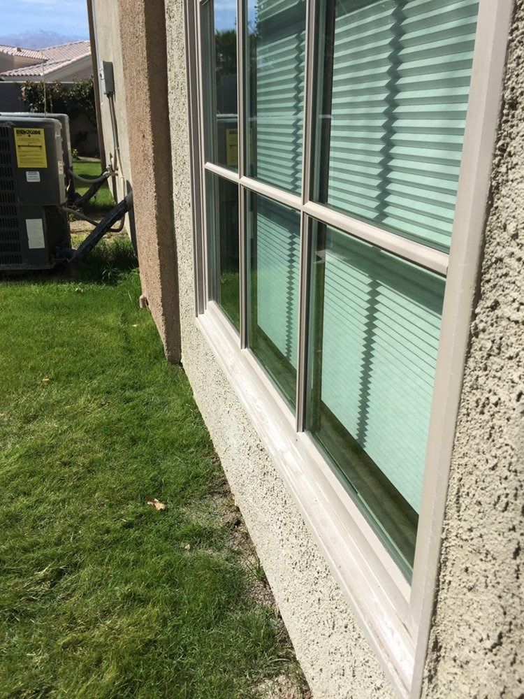 Exterior window with white trim and green blinds beside a grassy lawn