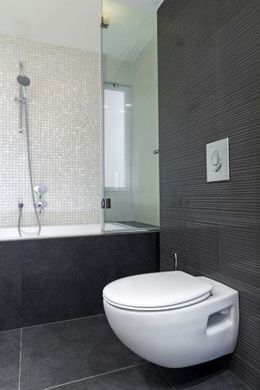 Modern bathroom with a wall-mounted white toilet, black tiled floor, and glass shower enclosure