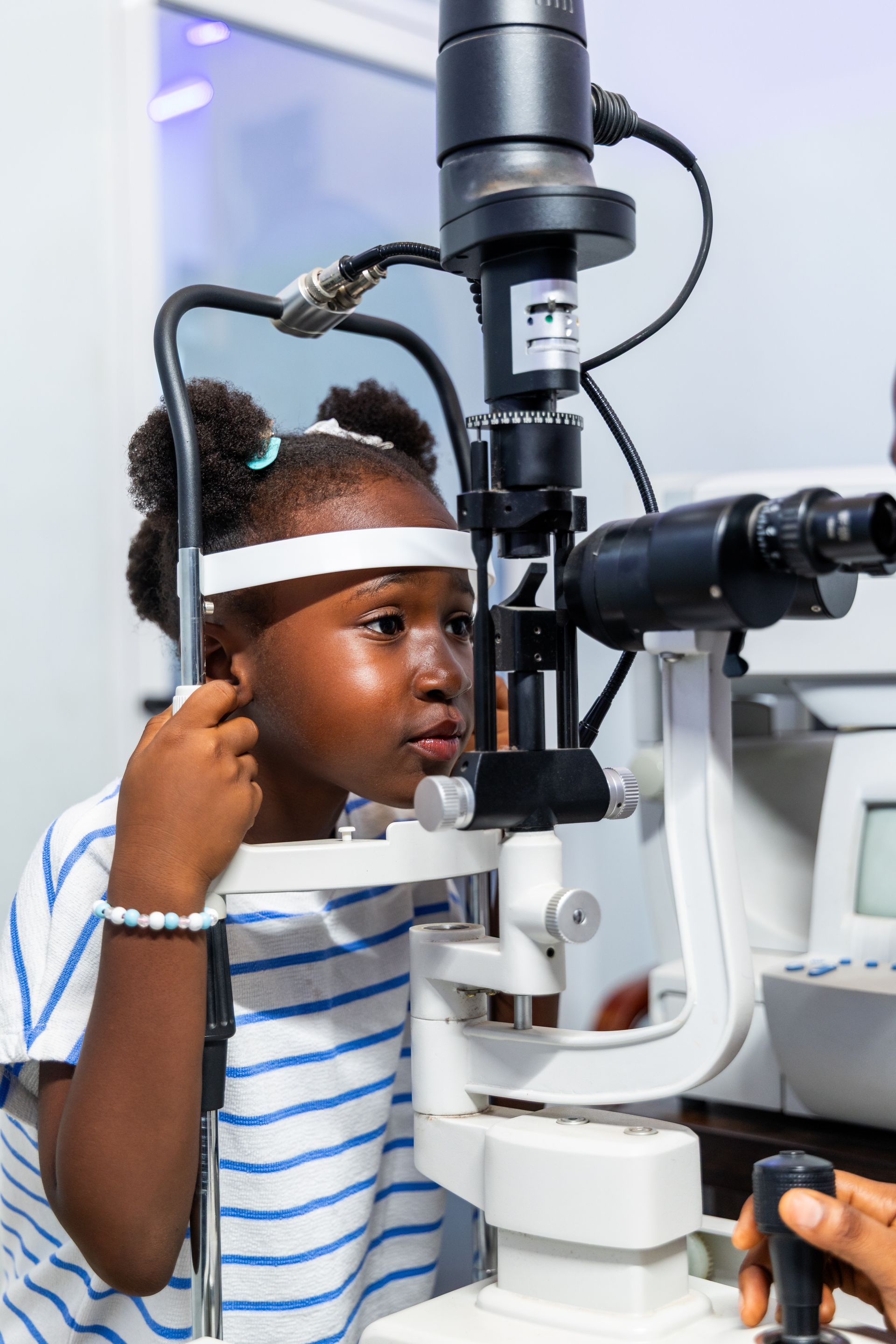 Pediatric eye doctor performing a vision exam for a young child using a slit lamp microscope.