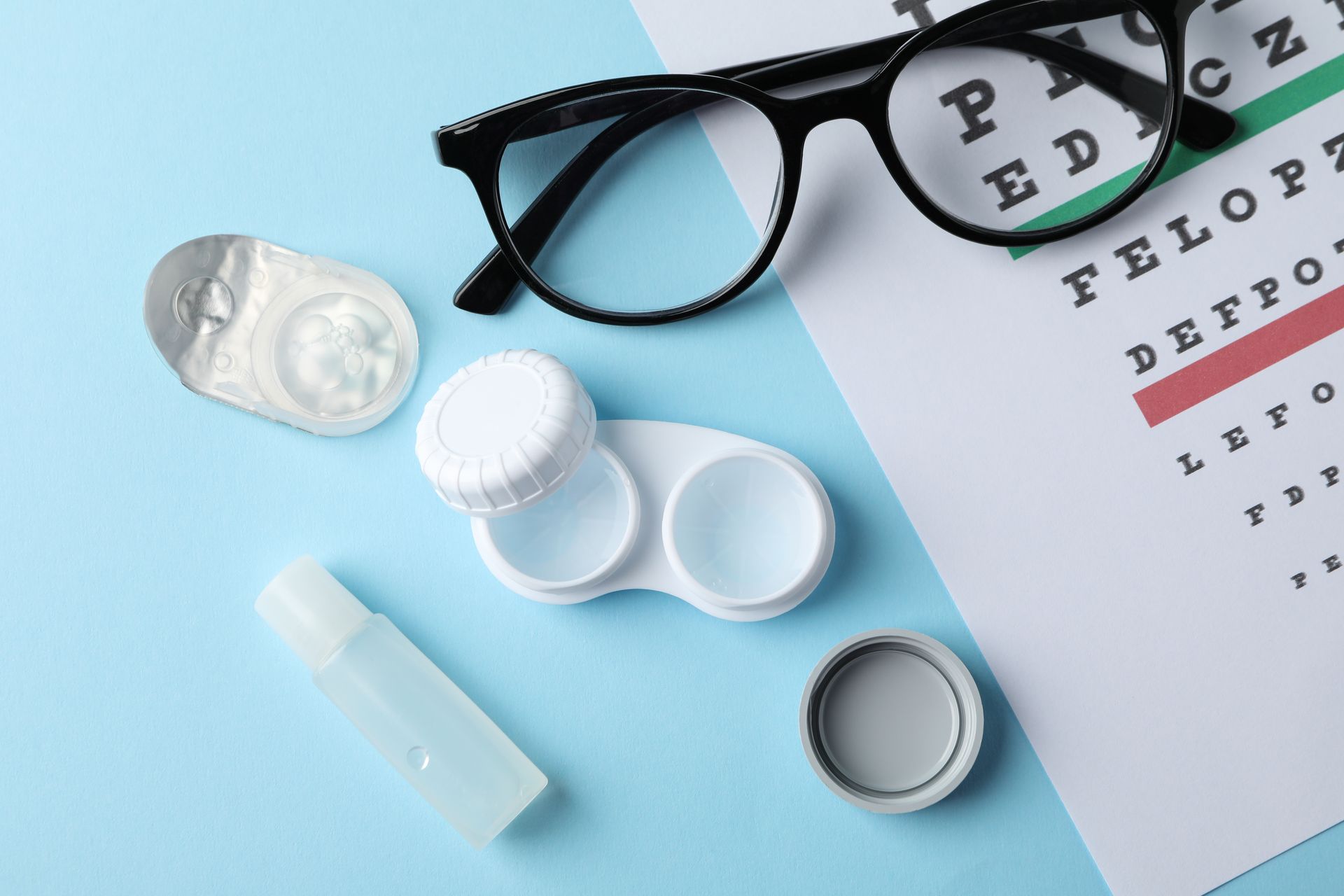 Glasses, contact lenses and eye test chart on blue background, top view Glasses, contact lenses and eye test chart on blue background, top view