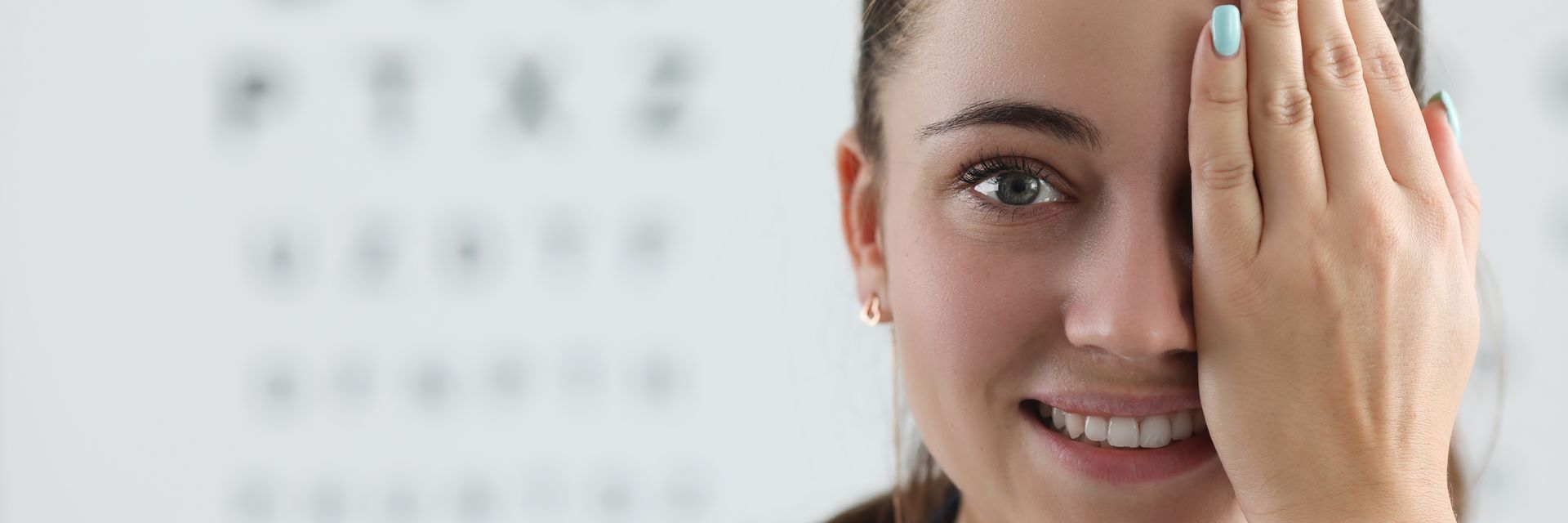 Smiling woman covering one eye during an eye exam with a vision chart in the background