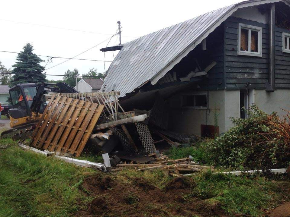 Une maison est en train d'être démolie avec un bulldozer en arrière-plan