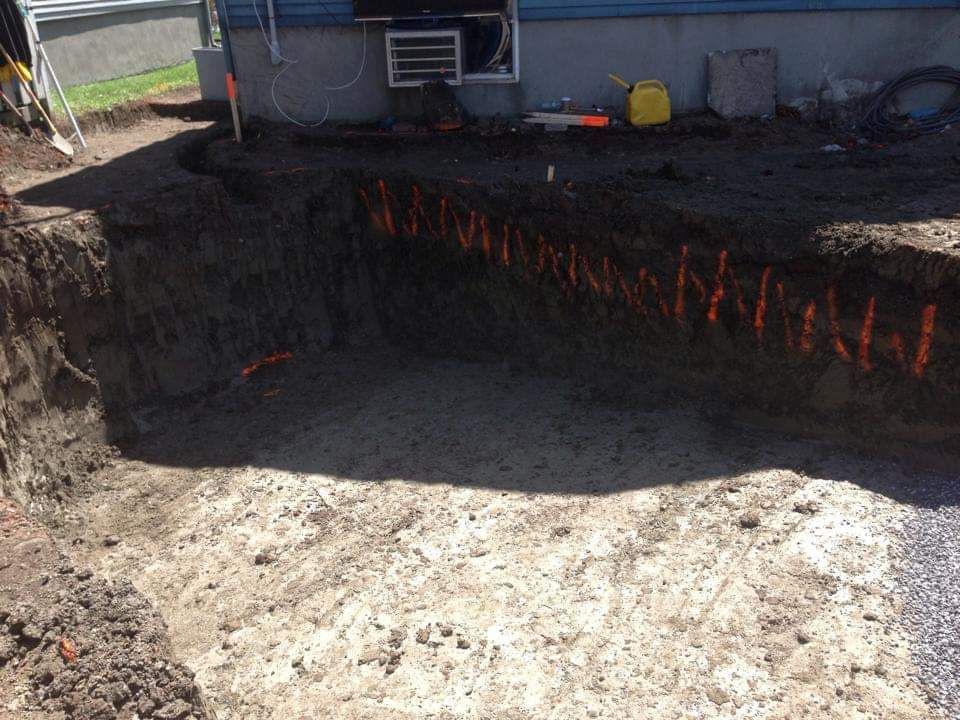 Un grand trou dans le sol est en train d'être creusé devant une maison.