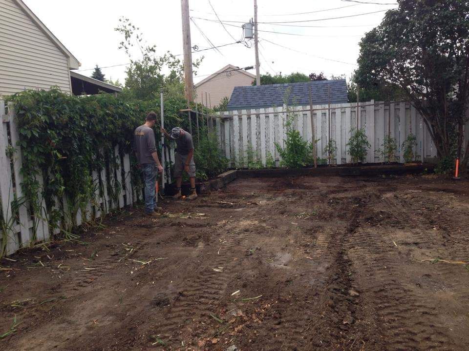 Deux hommes creusent la terre devant une clôture blanche.