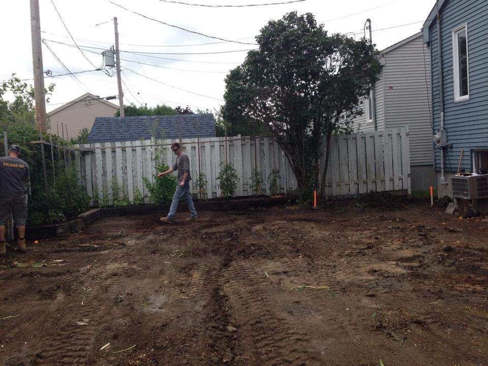 Un homme marche dans un terrain en terre battue devant une maison.